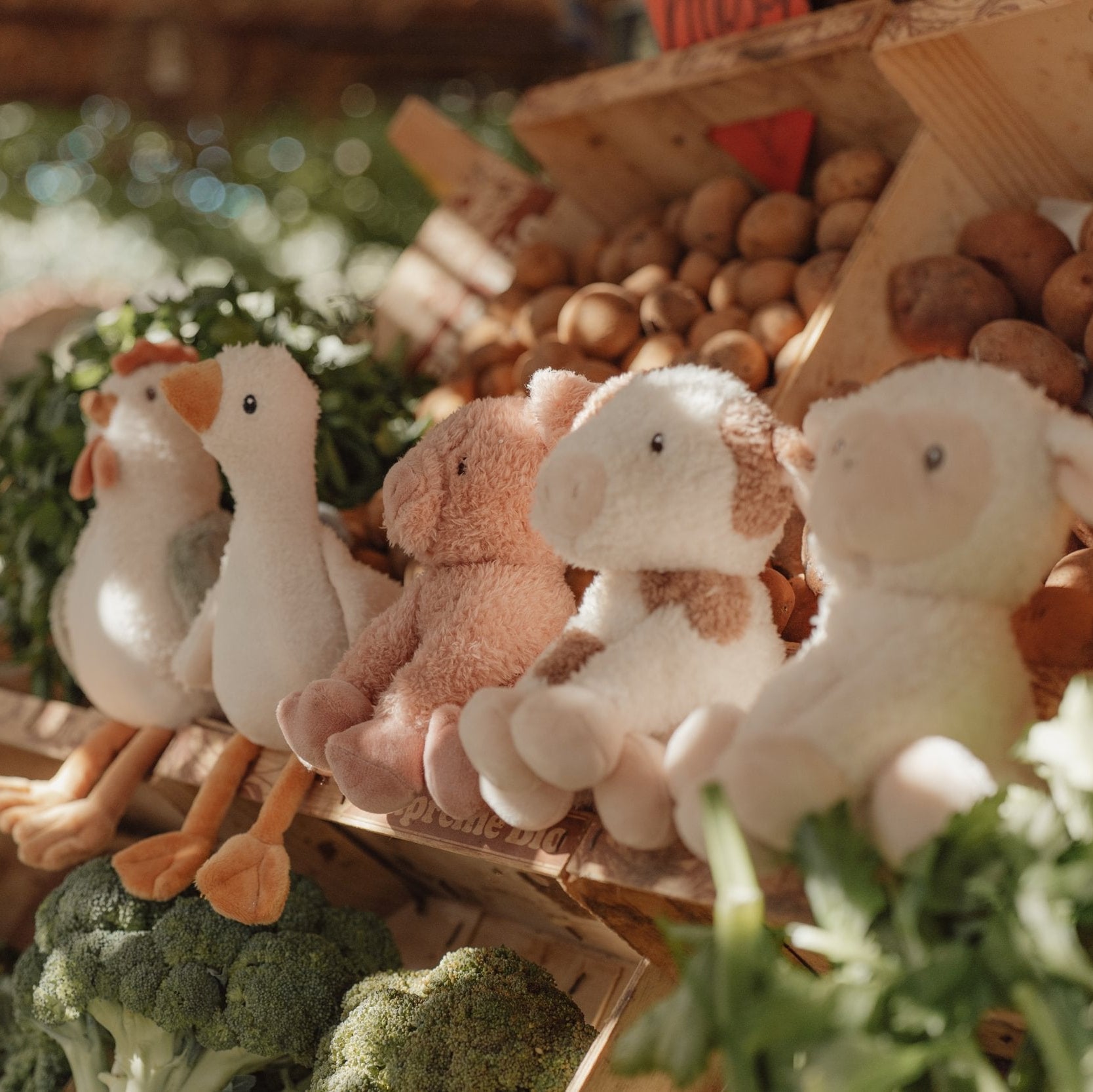 Plush toys resembling a duck, sheep, and cow on a wooden stand with vegetables in the background.