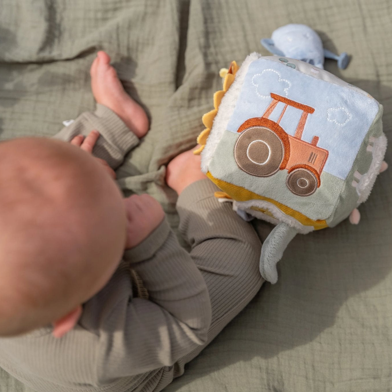 Baby lying on a blanket with a soft toy featuring a tractor design.