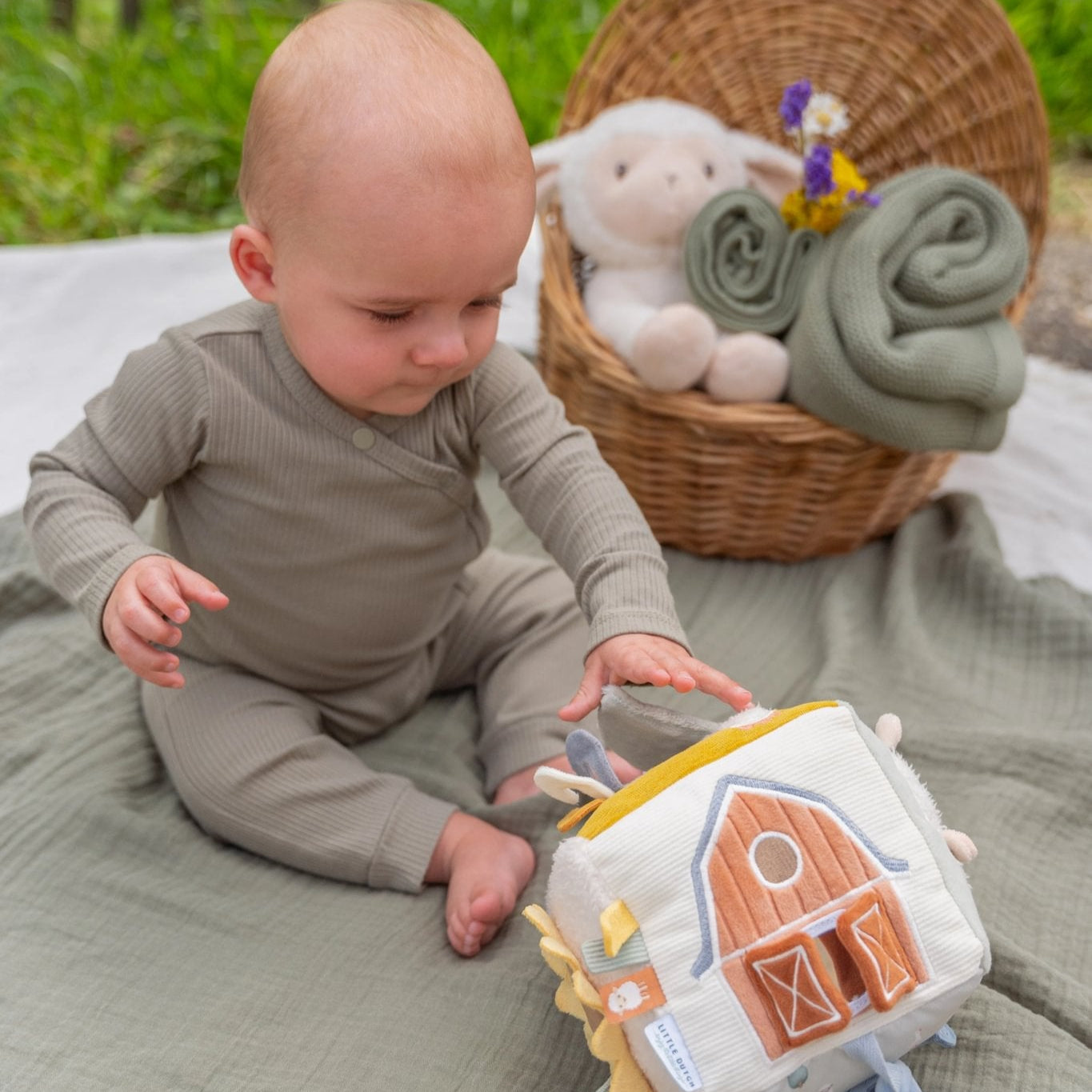 Baby playing with a soft toy on a blanket outdoors