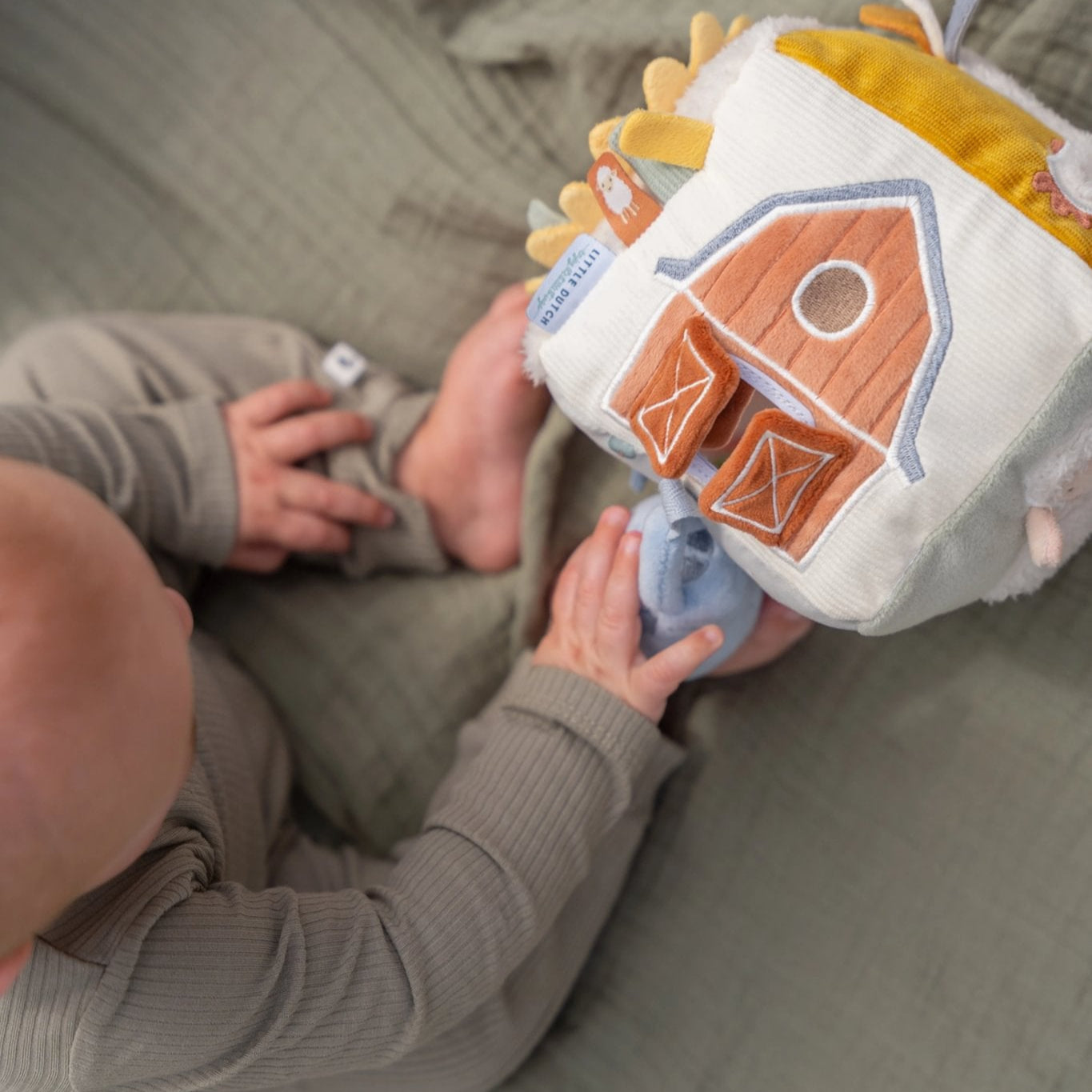 Child playing with a plush toy resembling a barn on a bed