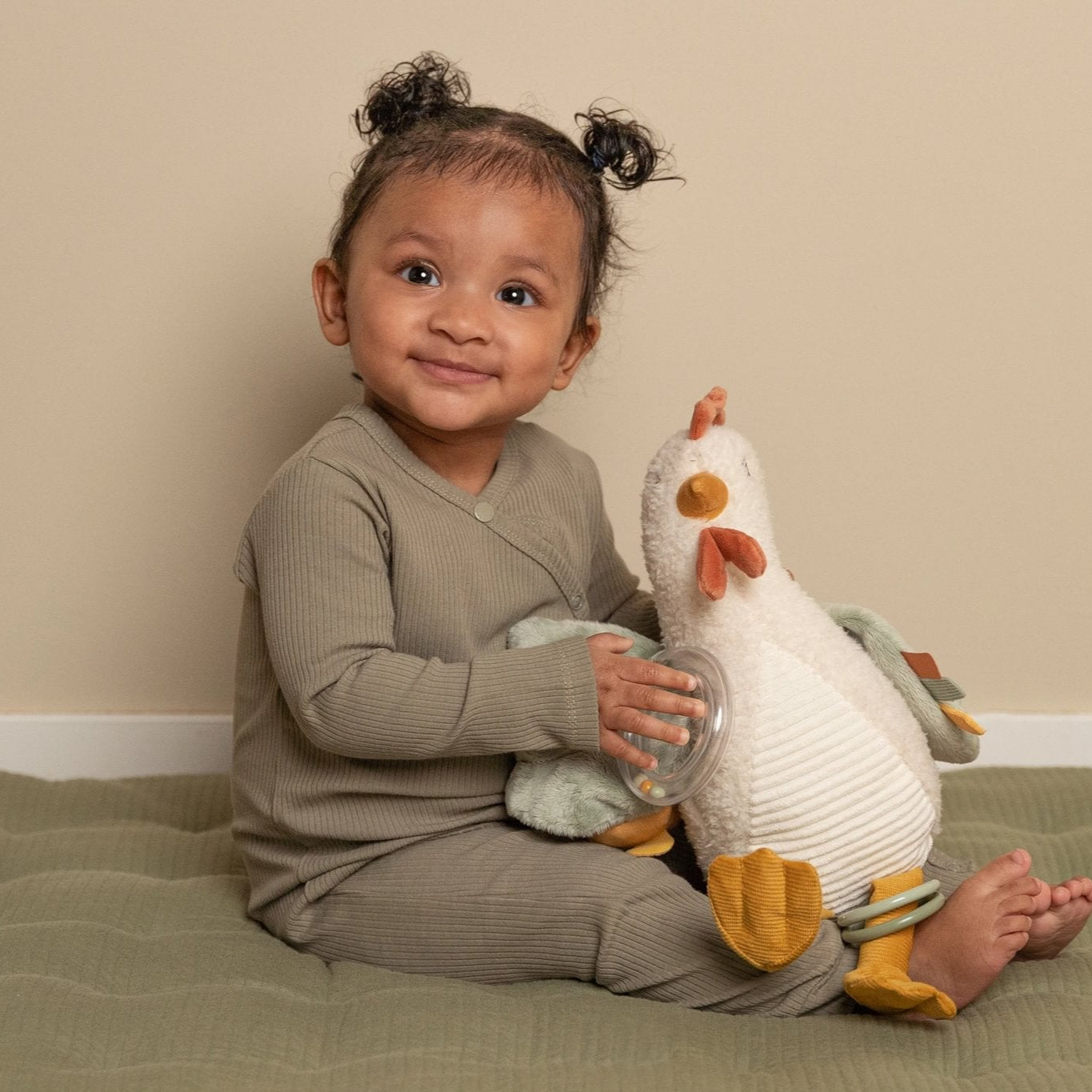 Child holding a plush toy on a bed with a plain background