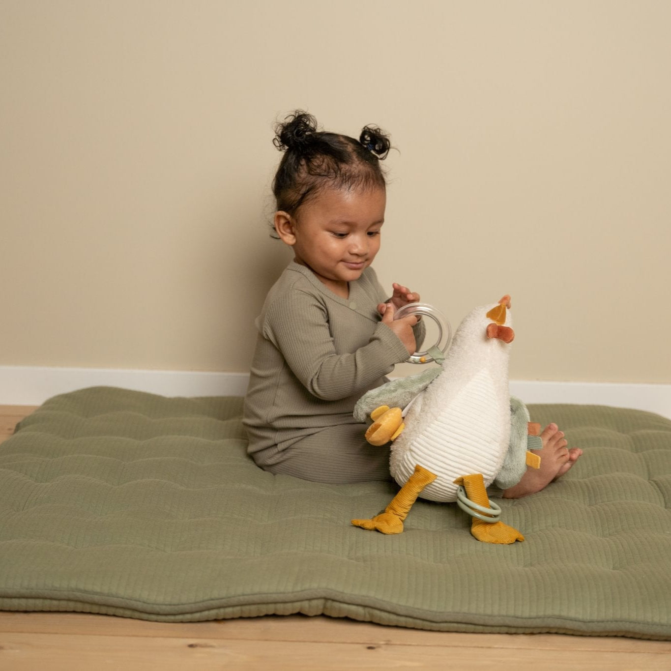 Child playing with a toy goose on a green mat in a room.