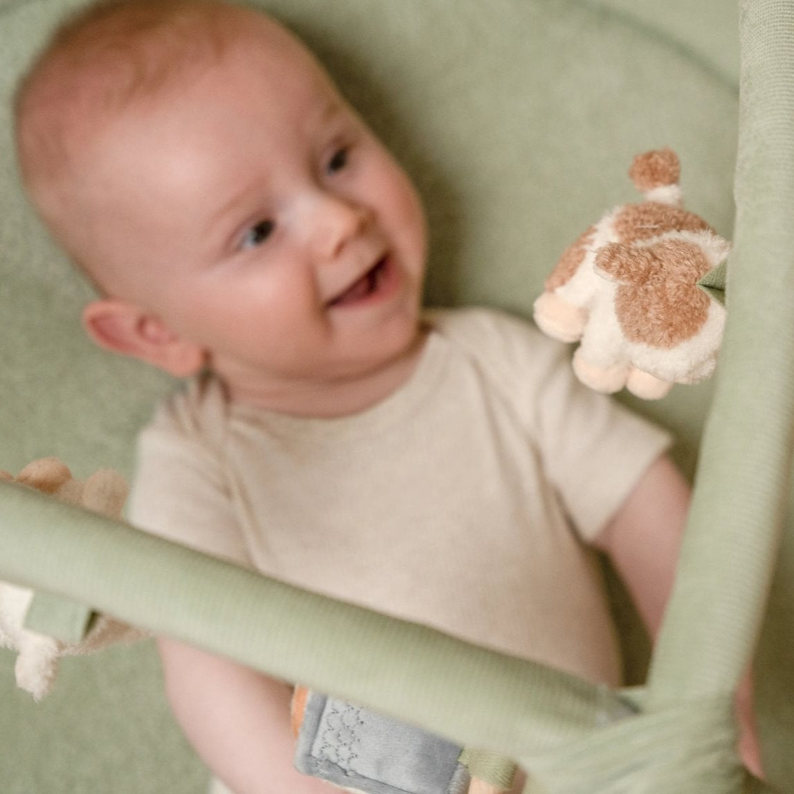 Baby in a green baby bouncer holding a plush toy