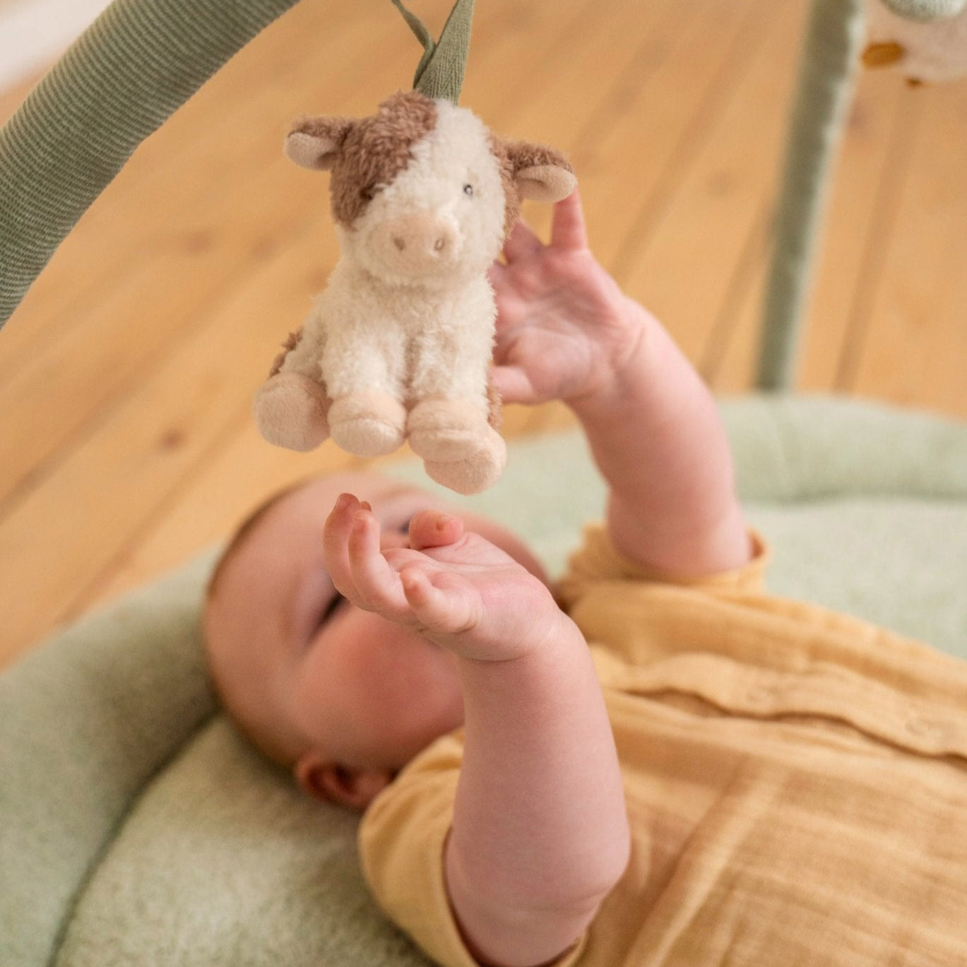 Baby reaching out to a hanging plush toy in a crib