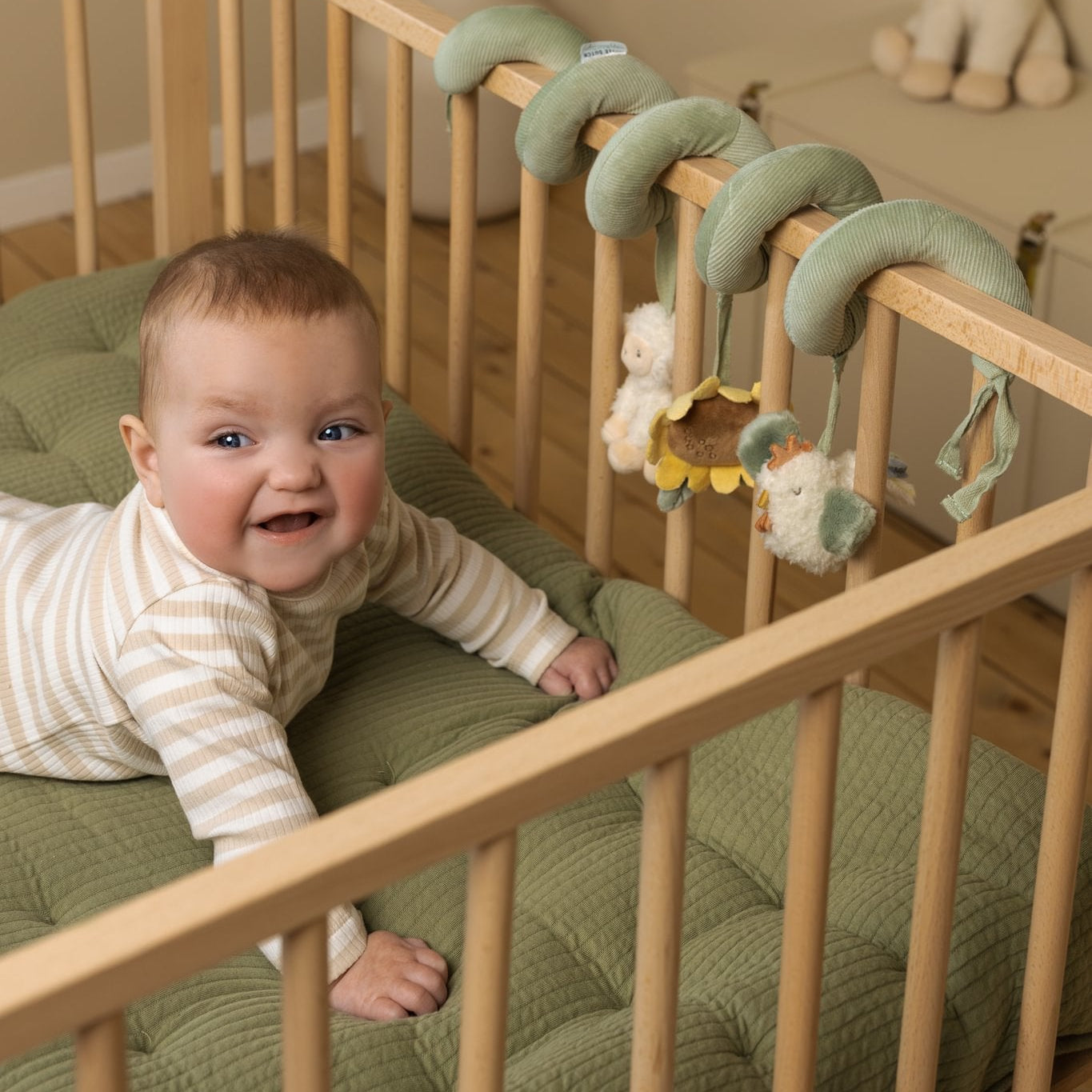 Baby in a crib with a wooden crib and green bedding, smiling at the camera.