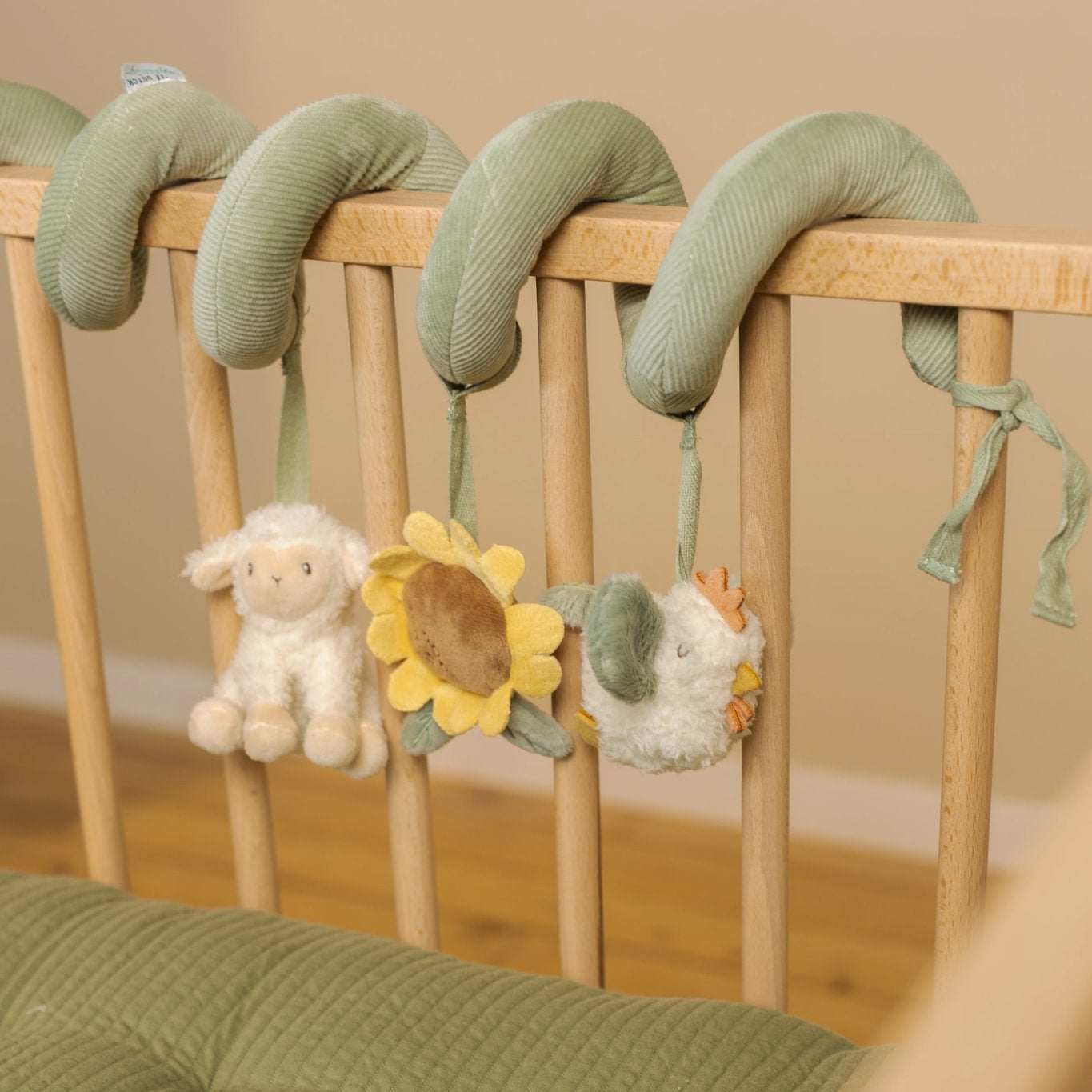 Crib with green crib mobile and toys against a beige wall.