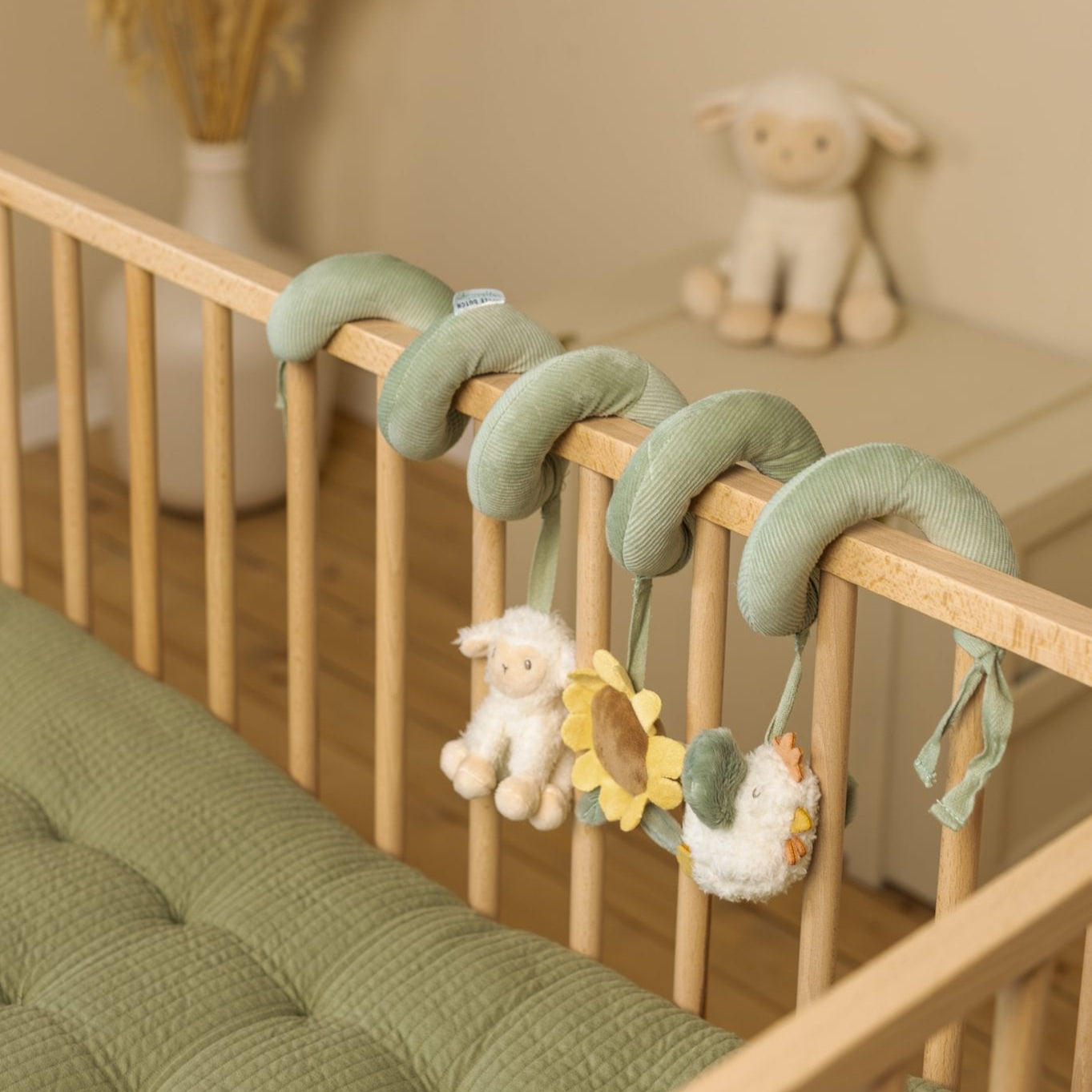 Wooden crib with green crib mobile and soft toys in a nursery setting.