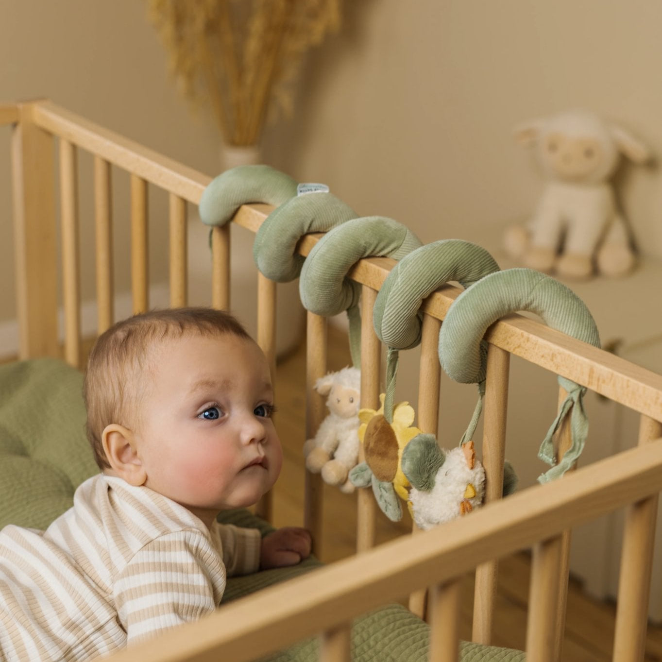 Baby in a crib with a mobile and stuffed toys, surrounded by greenery and soft lighting.