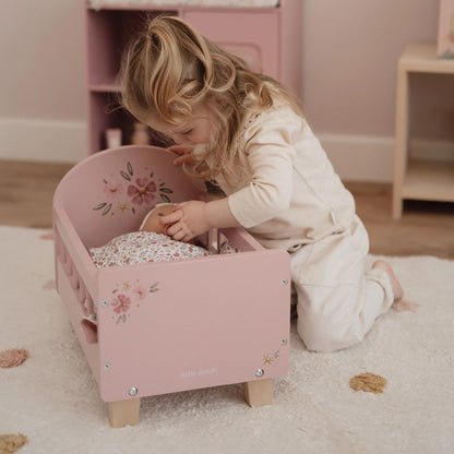 Child playing with a pink doll bed in a room with light-colored walls and wooden floor.