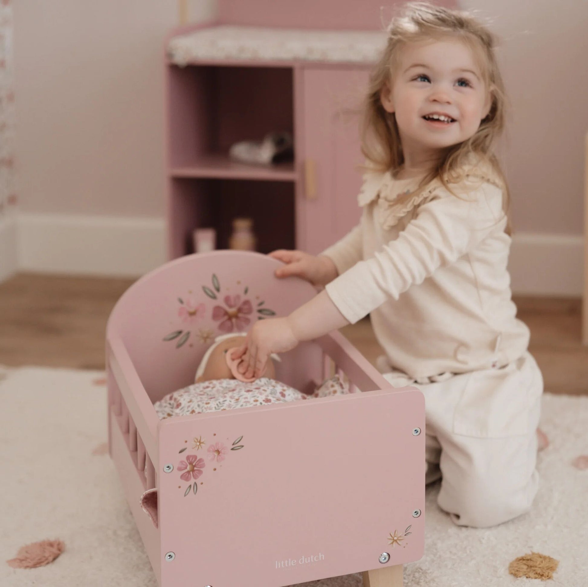 Child playing with a pink toy bed in a room with pink furniture.