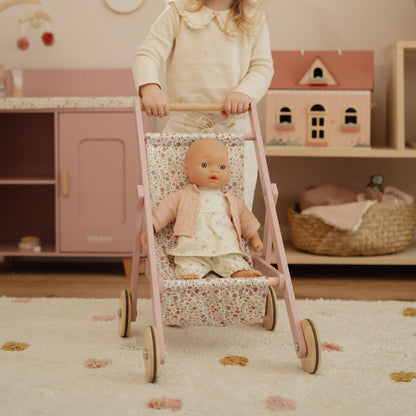 Child pushing a doll in a wooden pink stroller in a playroom setting