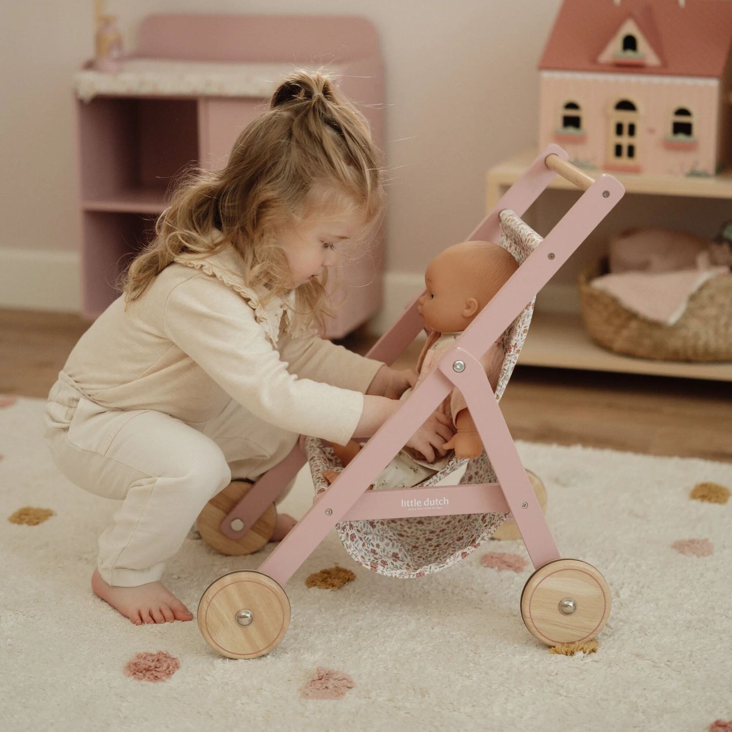 Child playing with a doll in a pink toy stroller in a cozy room.