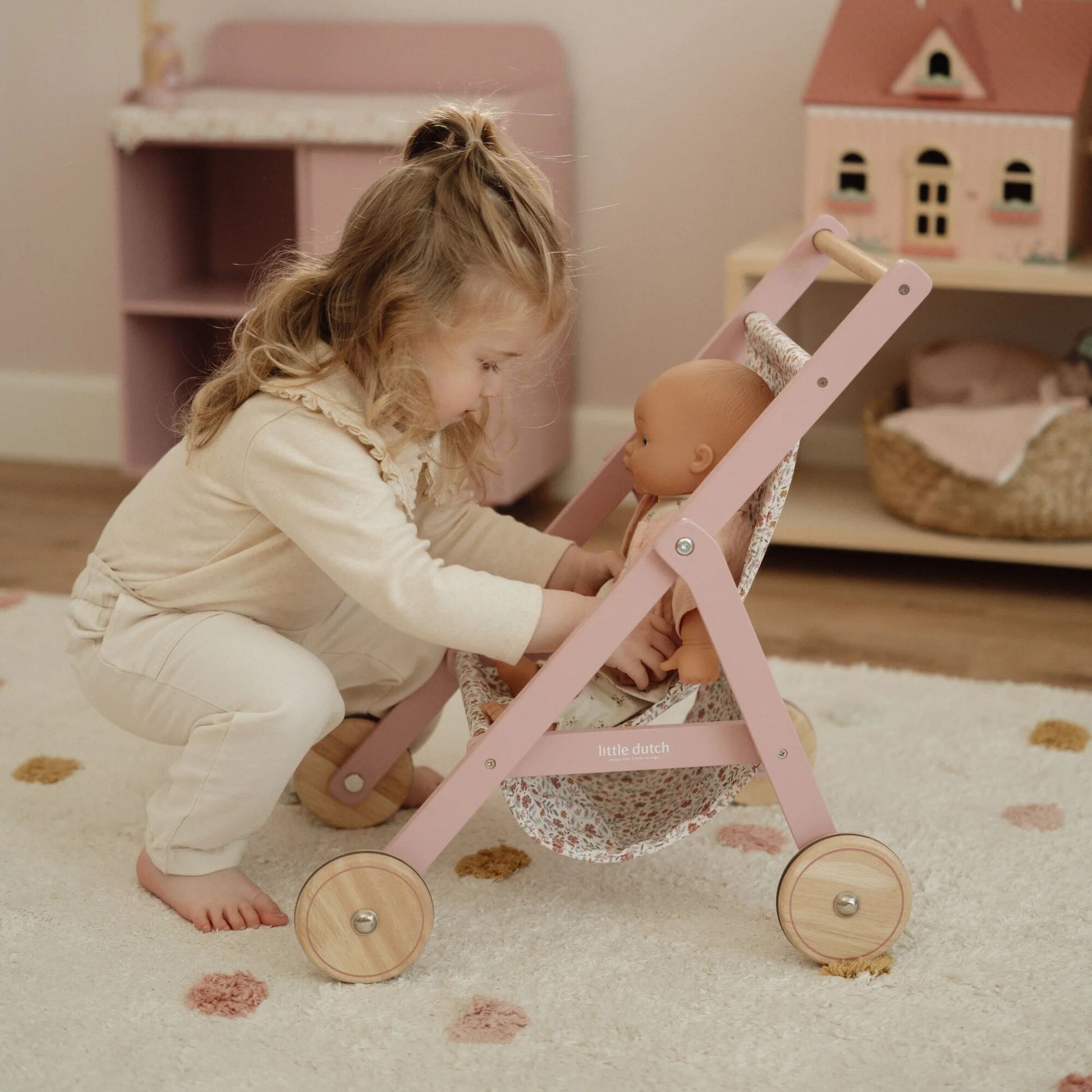 Child playing with a doll in a pink toy stroller in a cozy room.