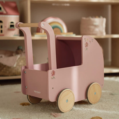 Pink toy pram with wooden wheels and handle in a child's playroom setting.