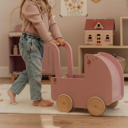 Child pushing a pink doll pram in a room with a toy house in the background