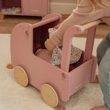 Pink doll stroller with a doll inside, on a carpeted floor.