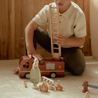 Child playing with wooden toy truck and figures on a carpeted floor.