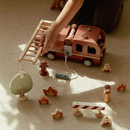 Child playing with wooden toy fire truck and accessories on a carpeted floor