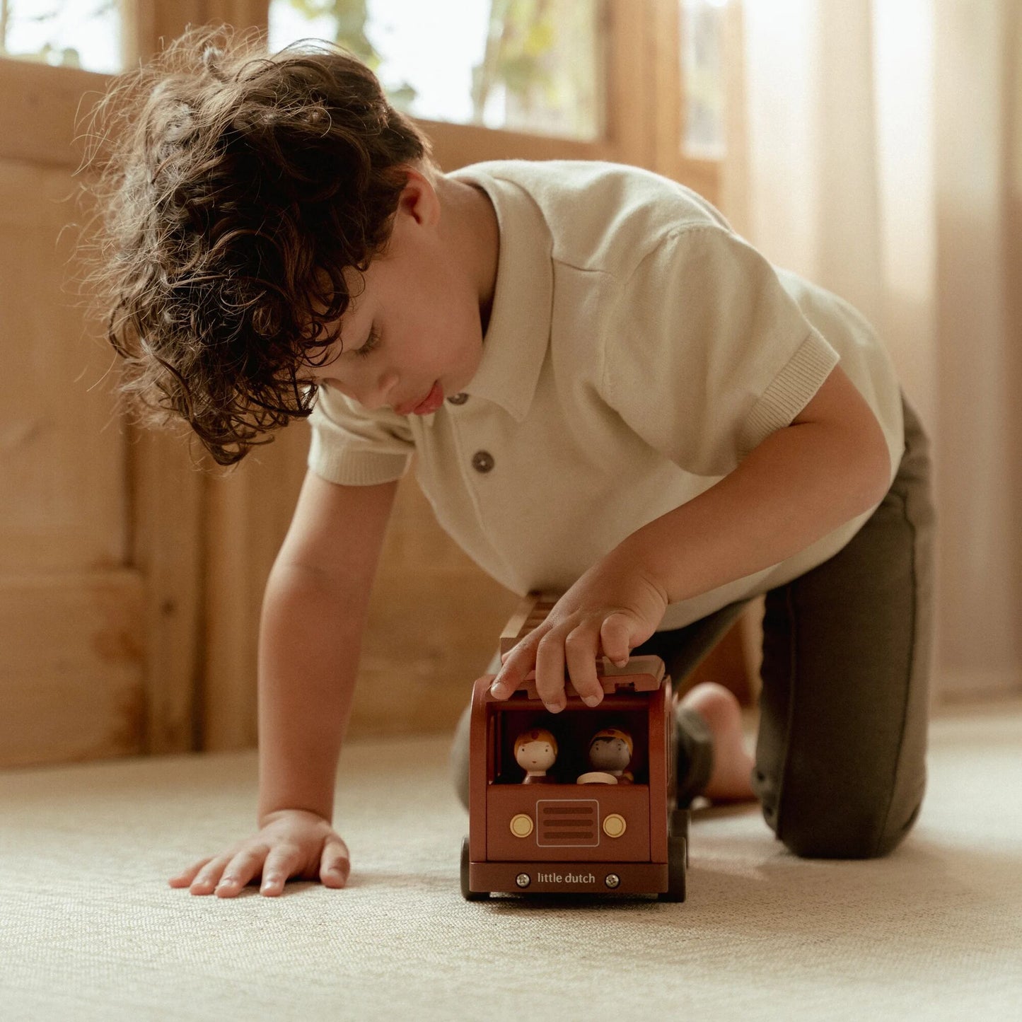 Child playing with a toy firetruck & firemen on a carpeted floor