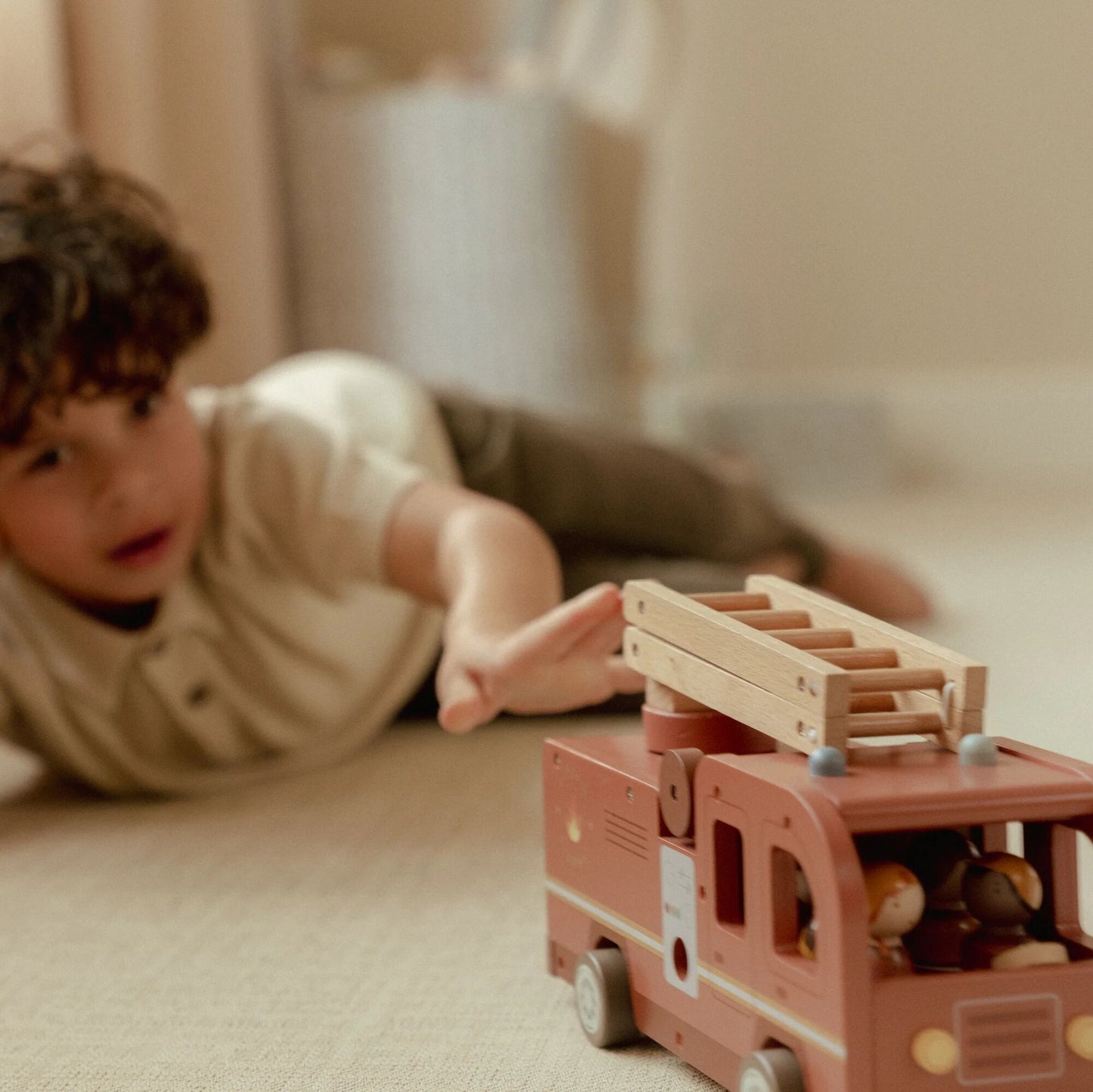 Child playing with a wooden toy fire truck on a carpeted floor.