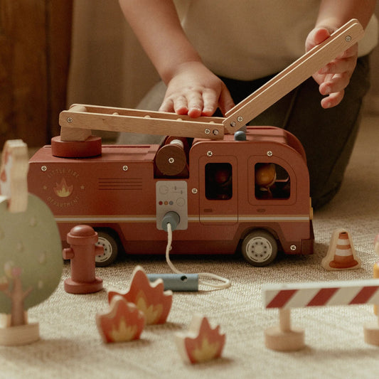 Child playing with a wooden toy fire truck on a carpeted floor.