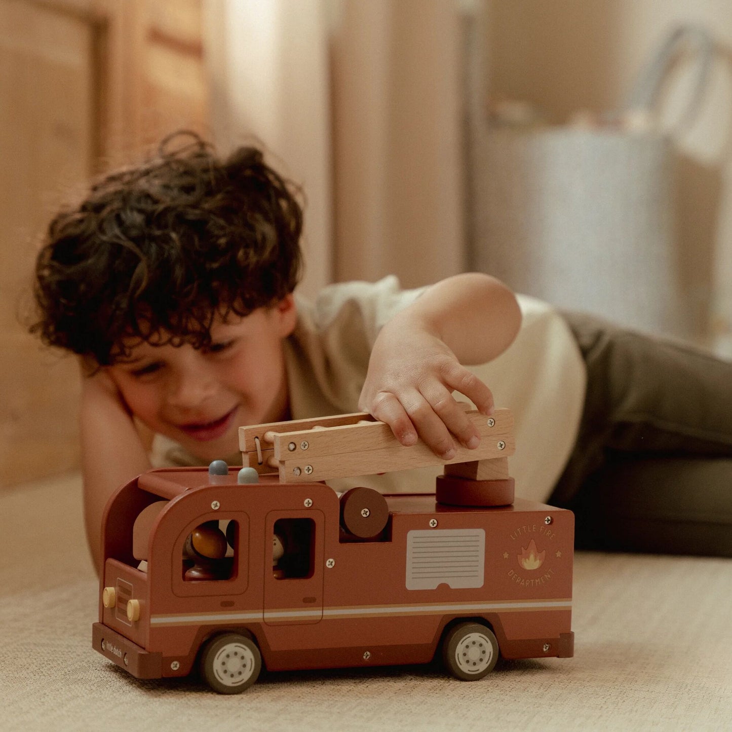 Child playing with a wooden toy truck on a carpeted floor.