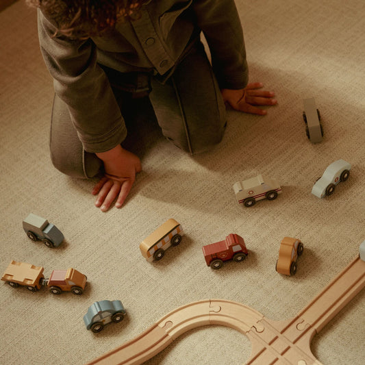 Child playing with wooden toy cars on a carpeted floor