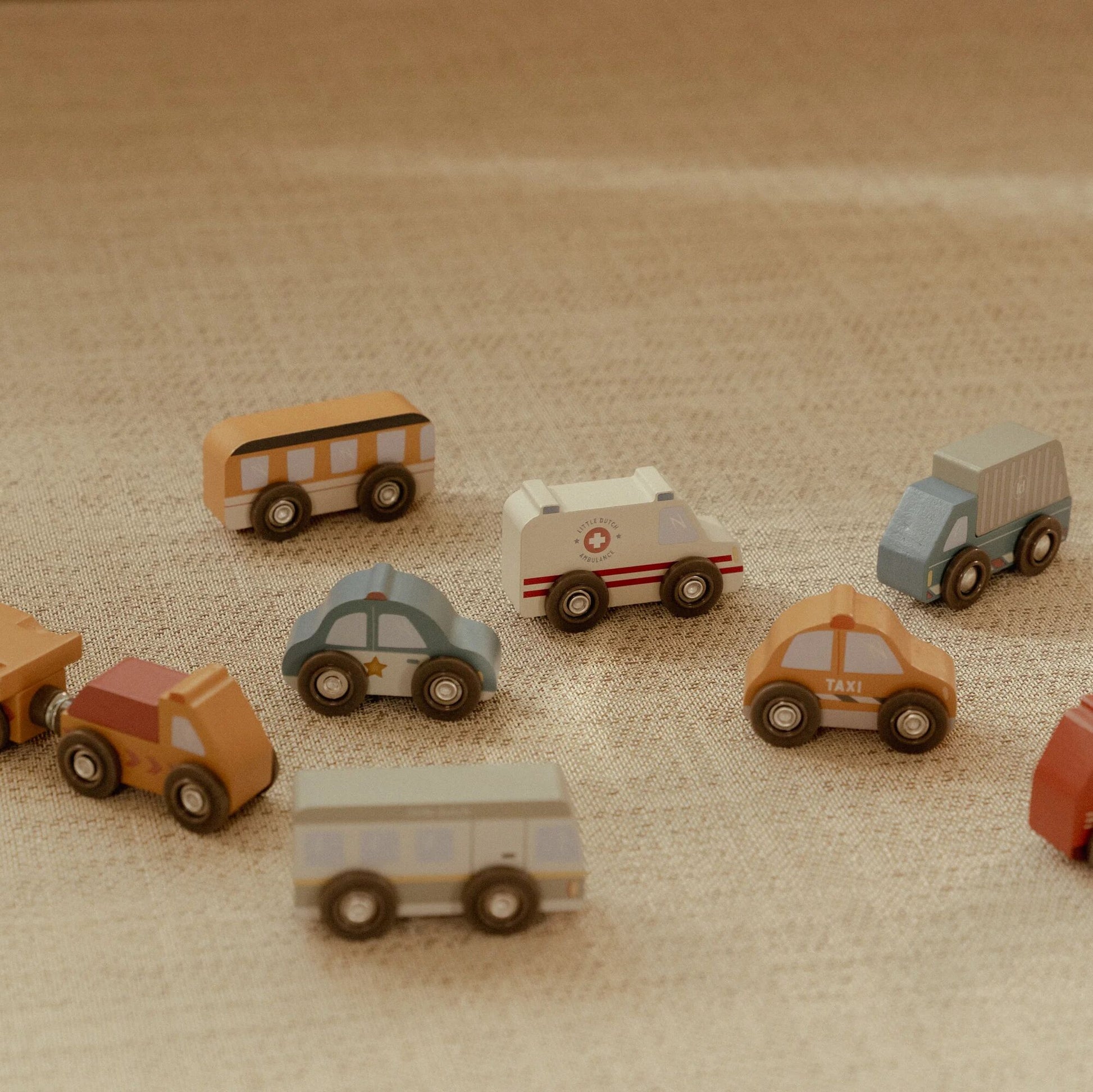 Set of toy vehicles including a bus, cars, and an ambulance on a textured surface.