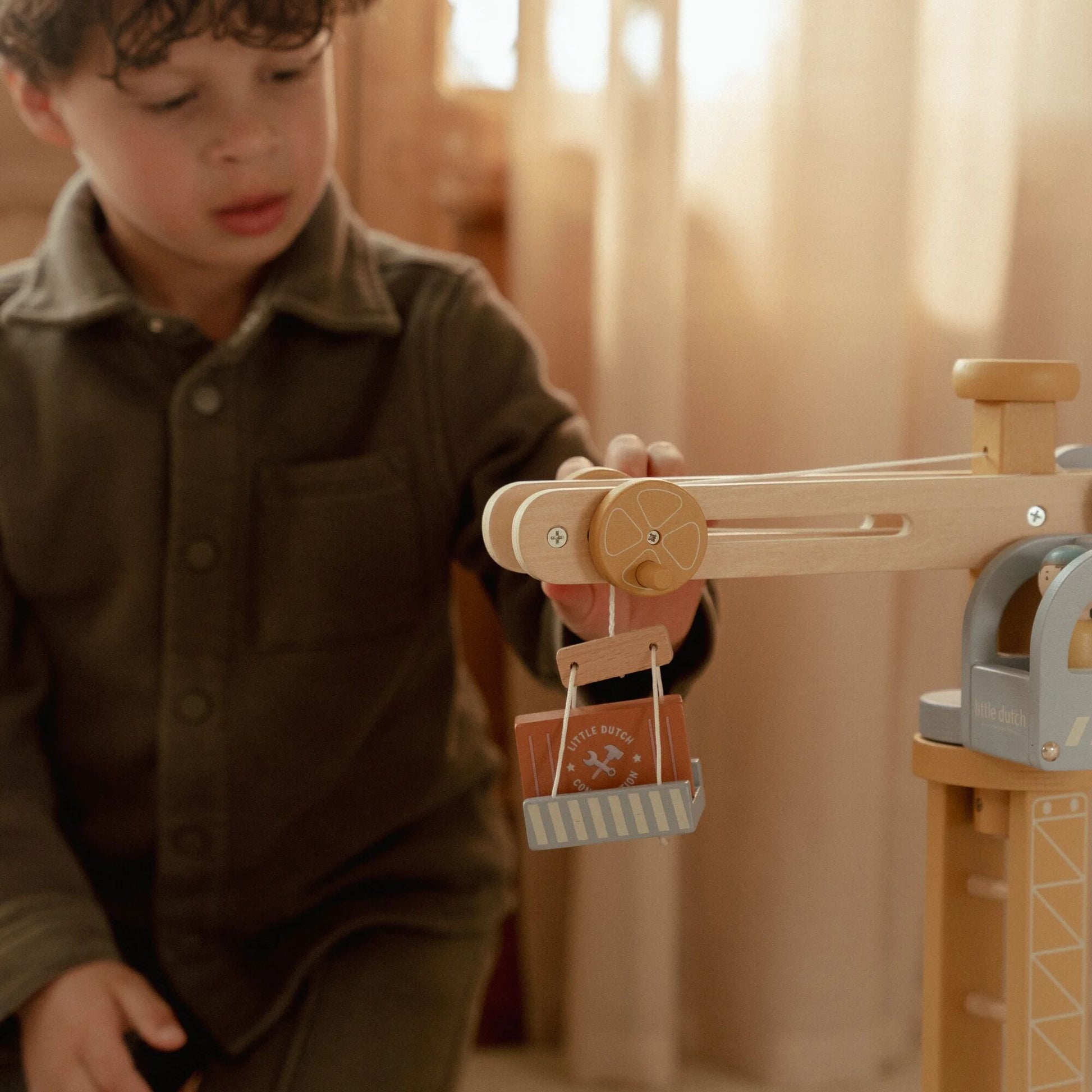 Child playing with a wooden toy crane in a warm indoor setting