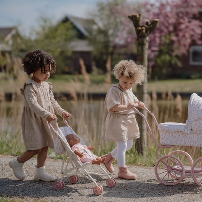 Two young girls playing with dolls and vintage-style strollers in a garden.